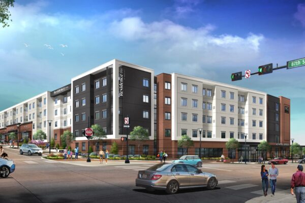 A modern, multi-story apartment complex situated at a busy intersection with shops on the ground floor. People are walking on sidewalks and crossing the street while cars and a bus are on the road. A street sign indicates the location as the corner of 87th Street Parkway.