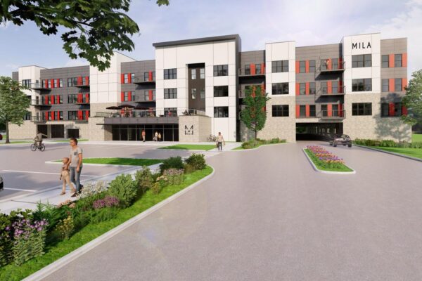 A modern four-story apartment building with a mix of white and gray exterior and red window accents. The building is labeled "MILA." There are people walking, biking, and landscaping around the entrance, with greenery, flowers, and a parking area in the foreground.