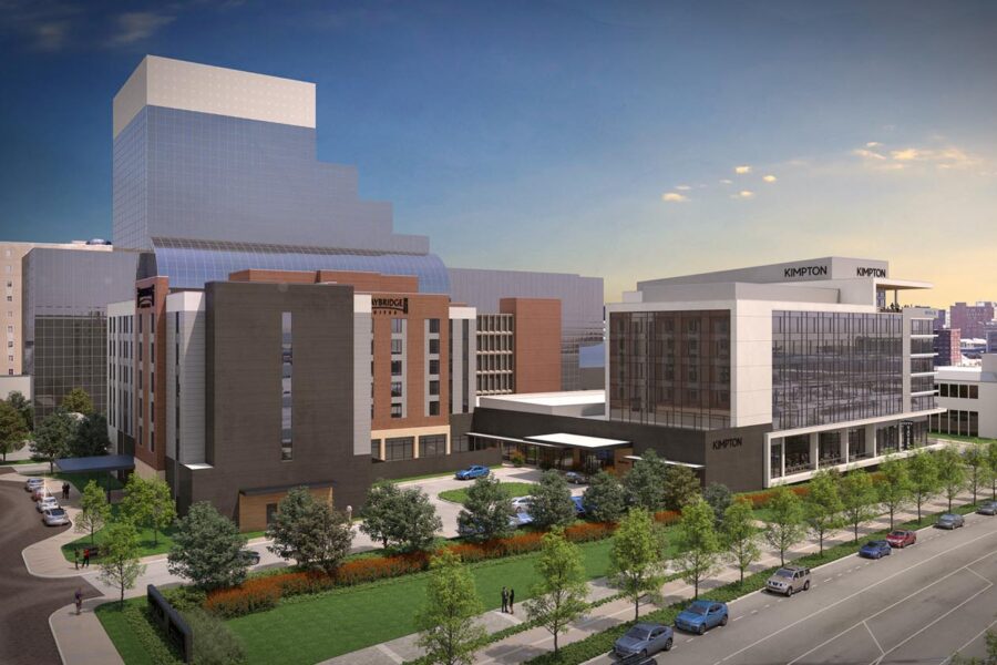 A modern urban landscape featuring multiple buildings, including two prominently marked with "Experion." The area is surrounded by greenery, trees, parked cars, and intersecting streets. The architecture displays a blend of glass and brick facades.